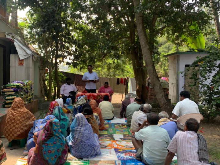 Elderly people seated on mats under trees at a gathering