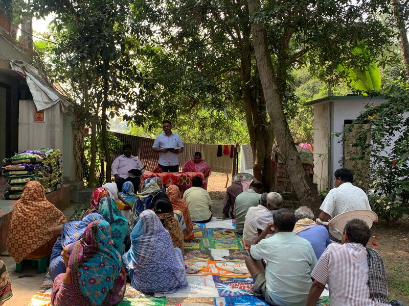 Elderly people seated on mats under trees at a gathering