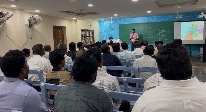 Pastors seated on benches at a training session, seen from the back