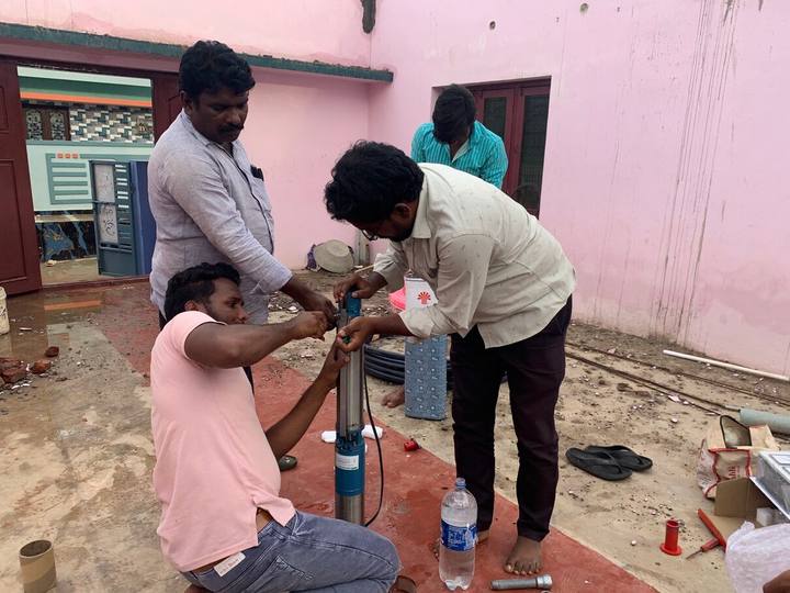 A group of men fitting a submersible pump in a courtyard
